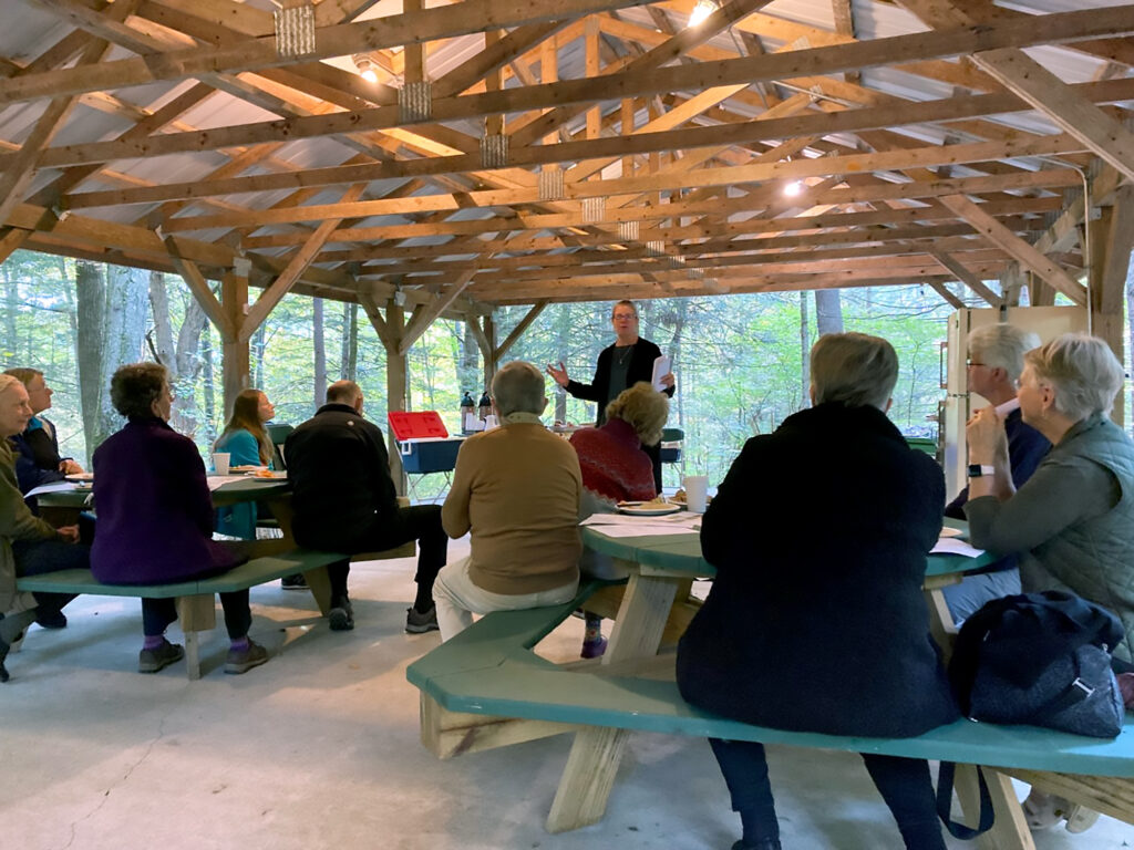 Chloe Learey gives a presentation to many people sitting in an outdoor wooden pavilion