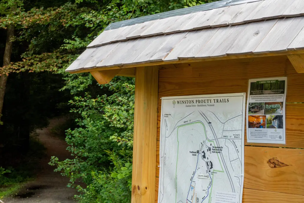 A wooden trailhead sign stands in front of entrance to trail